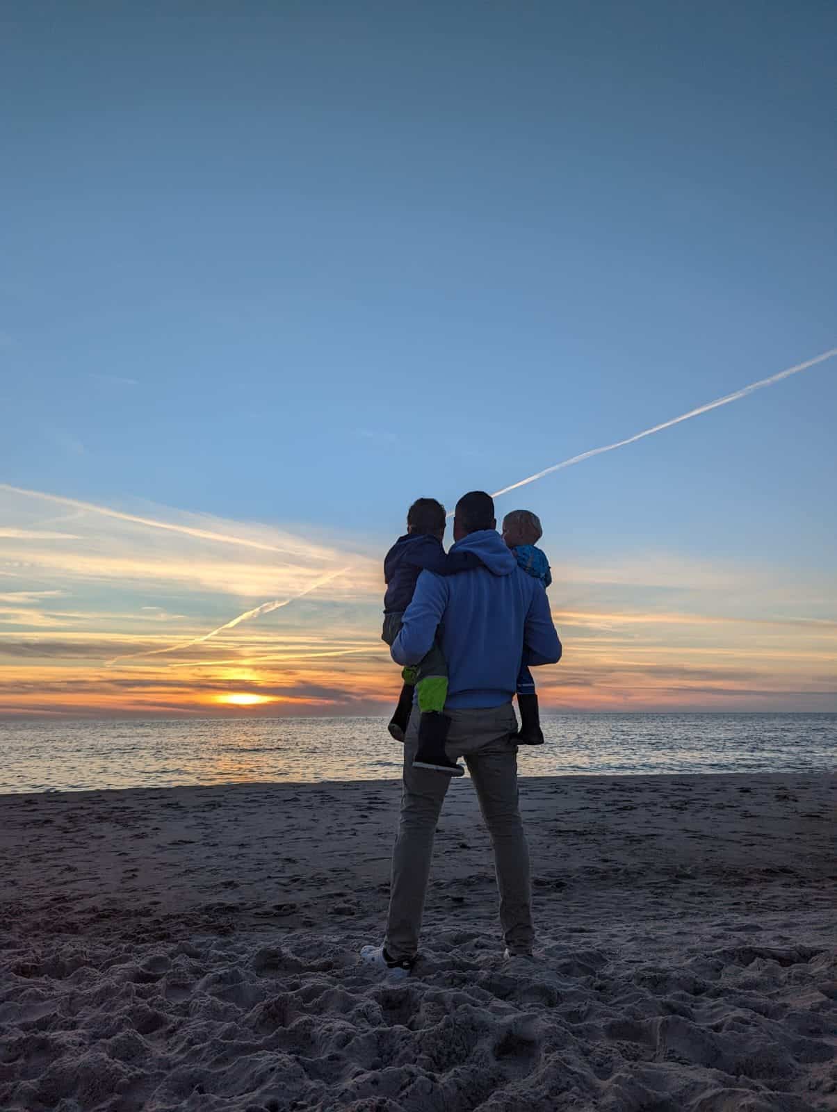 Christopher Redenz mit zwei Kindern am Strand bei Sonnenuntergang, von hinten